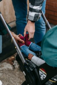 Caring parents adjusting their toddler's attire in a stroller during a walk on a sidewalk.